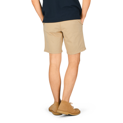 A person standing, wearing khaki beige Paige Phillips shorts and tan shoes, with a dark-colored top, viewed from the waist down.