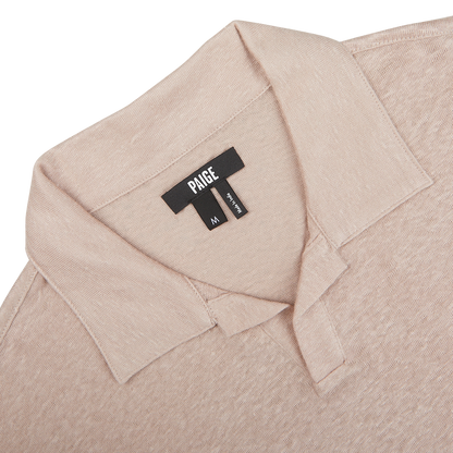 Close-up of a Light Pink Linen Capri Collar Polo Shirt's label with the brand "Paige" and size "M" on a light background.
