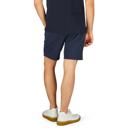Man standing wearing Paige navy blue cotton blend Phillips shorts and white sneakers with yellow soles.