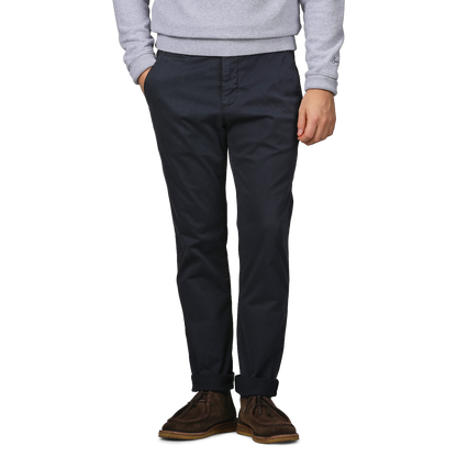 A person dressed in a gray sweater, Paige's Navy Blue Danford Cotton Chinos, and brown shoes stands with hands in pockets, highlighting a comfortable fit.