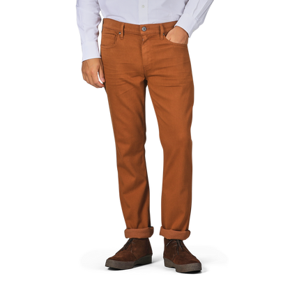 A person wearing a white shirt and Paige Rust Brown Cotton Transcend Federal Slim Jeans rolled up at the cuffs, paired with brown shoes. The head is not visible in the image, but the comfortable fit of the outfit suggests ease and style.