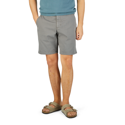 Man in a blue t-shirt and Slate Grey Cotton Blend Phillips shorts by Paige, wearing beige sandals, standing on a yellow textured surface.