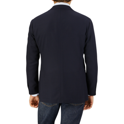 Rear view of a man wearing a Ring Jacket Navy Blue Wool Balloon Travel Blazer and jeans, standing against a light grey background.