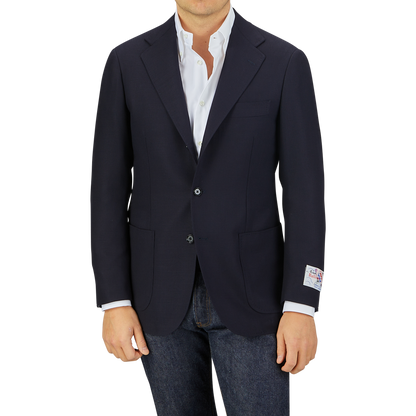 Man wearing a Ring Jacket Navy Blue Wool Balloon Travel Blazer over a white shirt paired with jeans, standing against a gray background.