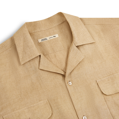 A Beige Linen Army Shirt by Maurizio Baldassari lies flat on a white background. It has a spread collar, cream buttons, and two flap chest pockets. The inner label notes the designer and that it’s made in Italy. , available at Richard Gelding Mayfair