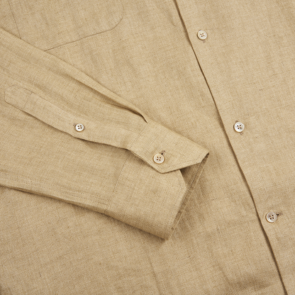 A close-up of the Maurizio Baldassari Beige Linen Army Shirt highlights the textured fabric, light buttons, chest pocket, clean stitching, and a long sleeve with a buttoned cuff laid flat. , available at Richard Gelding Mayfair