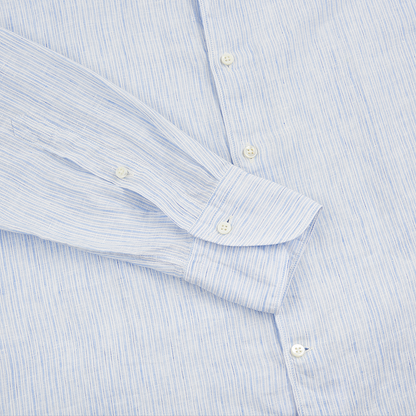 The Stenströms Blue Stripe Linen Slimline Shirt features light blue and white stripes, white buttons, a single-button cuff, and a soft, lightweight linen fabric. Its left sleeve is extended diagonally across the body in the image. , available at Richard Gelding Mayfair