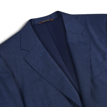 A close-up of the Canali Mid Blue Micro Design Wool Suit jacket showcases its notched lapel, dark navy lining, and refined tailored texture. Laid flat on a white backdrop, it highlights the elegance of men's formalwear. , available at Richard Gelding Mayfair