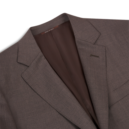 A close-up of the Canali Dark Brown Tropical Wool Suit highlights its notched lapel, chest pocket, visible brown lining, and a “MADE IN ITALY” collar tag. The fabric is smooth and finely woven. , available at Richard Gelding Mayfair