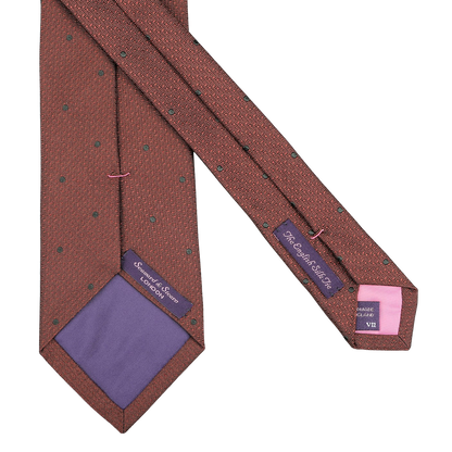 A close-up of a Seaward & Stearn Brick Orange Dot Silk Tie reveals two inner labels reading "St. George St. London" and "Handmade in England." The handmade silk tie features purple and pink lining at the tips, adding a touch of elegance.