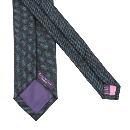 Introducing the Dark Blue Woven Wool Tie by Seaward & Stearn, featuring a rich dark blue design with a purple lining and adorned with two labels, one purple and one gray, at the ends. Handmade in England from pure wool, this exquisite accessory embodies refined elegance.