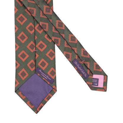 A Seaward & Stearn handmade silk tie, named the Green Orange Geometric Silk Tie, with a red geometric pattern on a dark background, featuring purple labels and a charming purple tip.