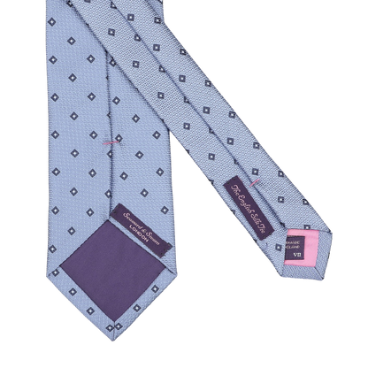 A Light Blue Diamond Woven Silk Tie by Seaward & Stearn, crafted in England from silk, features diamond patterns, a purple inner lining, and has the brand labels on the underside.
