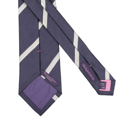 A navy blue silk tie with cream diagonal stripes, subtly showing pink labels inside, expertly handmade in England by Seaward & Stearn.