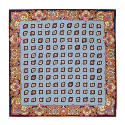 The Cardo Light Blue Silk Pocket Square by Sera Fine Silk features a square design with a light blue central area adorned with a repeating ornate pattern, surrounded by an intricate red and gold floral border and finished with hand-rolled edges.