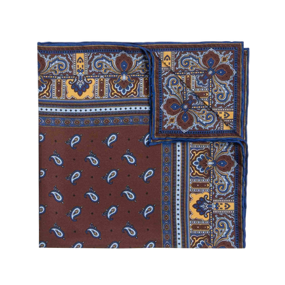 A neatly folded, square-shaped Chocolate Recioto Silk Pocket Square from Sera Fine Silk showcases a vibrant paisley pattern in blue, brown, and yellow tones with one corner visible. This luxury silk pocket square is made in Italy.