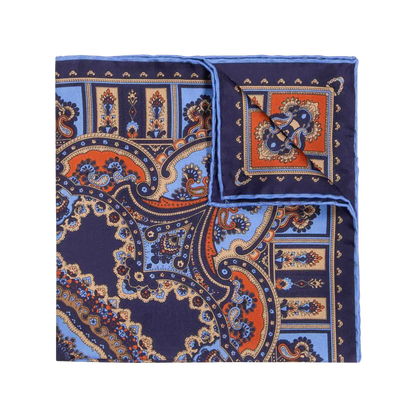 The Licorice Barolo Silk Pocket Square by Sera Fine Silk features an elaborate folded design with a navy blue paisley pattern, accented by orange and light blue hues. Crafted from pure Como silk, it boasts hand-rolled edges.