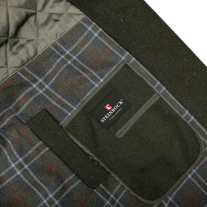 Close-up of a coat interior displaying a quilted lining and a fabric tag with the "Steinbock" label. The Dark Green Wool Alpaca Loden Coat, crafted from a wool-alpaca blend, features a plaid pattern in gray, red, and blue tones.