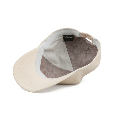 A cream microfibre baseball cap by Wigéns is displayed inside out, showing a brown sport twill lining, a black tag with white Wigéns script, an elastic back band, and visible brim stitching on a plain white background. , available at Richard Gelding Mayfair