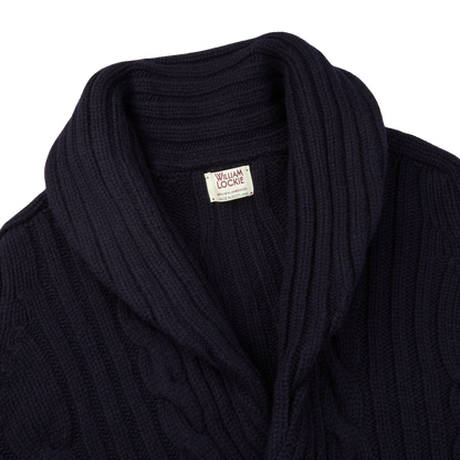 The William Lockie Navy Cable-Knit Lambswool Shawl Collar Cardigan, featuring a navy blue color and a cable-knit design, is displayed on a white background.