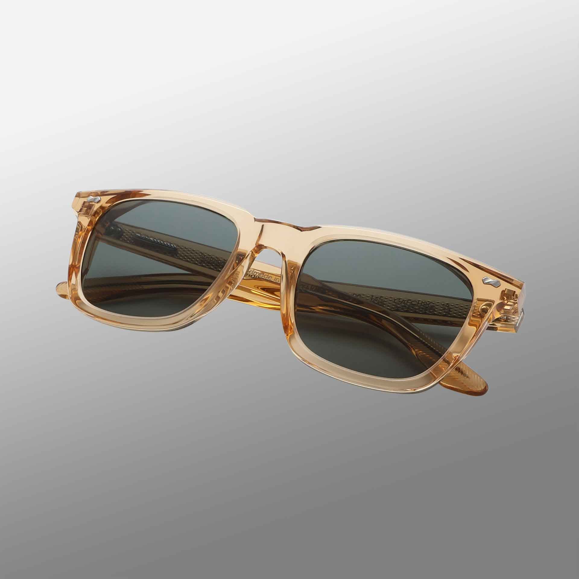 Carré Eco Champagne | Bottle Green sunglasses by TBD Eyewear feature transparent light brown rectangular frames, dark bottle green lenses, subtly patterned temples, and are shown over a smooth grey background with a faint shadow beneath. , available at Richard Gelding Mayfair