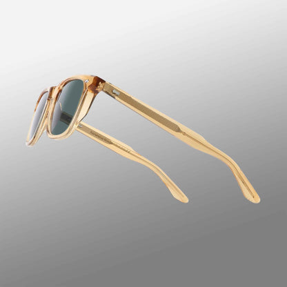 The Carré Eco Champagne | Bottle Green sunglasses by TBD Eyewear feature transparent amber frames and dark rectangular lenses, displayed angled on a gray gradient. Their slightly curved arms have a ribbed texture on the inner side. , available at Richard Gelding Mayfair