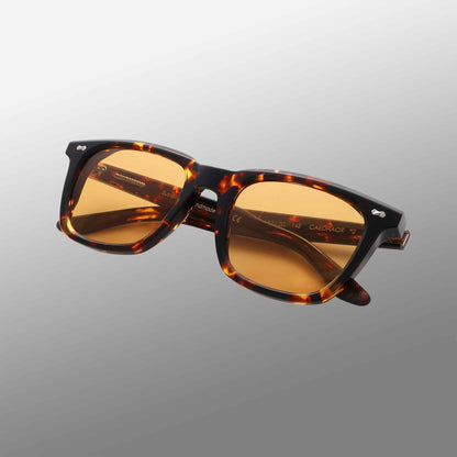 The Carré Eco Dark Havana | Orange sunglasses by TBD Eyewear feature a thick, tortoiseshell-patterned frame and rectangular amber-tinted lenses, showcased at an angle against a smooth gray gradient background. , available at Richard Gelding Mayfair