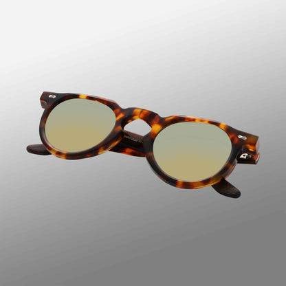 The Hem Eco Spotted Havana | Mirror Green sunglasses by TBD Eyewear feature thick acetate frames and silver hinge accents. Displayed at an angle on a gradient gray backdrop, they highlight both the front and side profiles. , available at Richard Gelding Mayfair