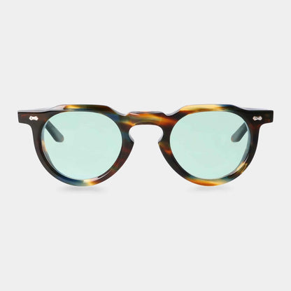 The Hem River | Light Green sunglasses by TBD Eyewear feature thick, round tortoiseshell-patterned frames, green-tinted lenses, a keyhole bridge, and small silver accents by the hinges. Shown on a plain white background. , available at Richard Gelding Mayfair