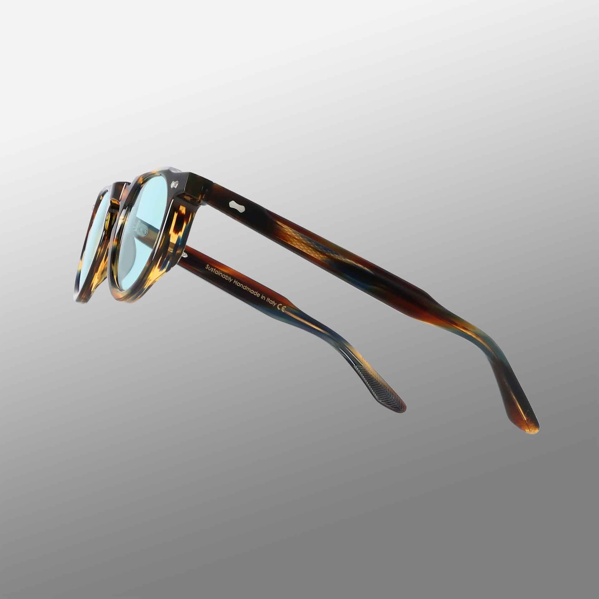 Hem River | Light Green eyeglasses by TBD Eyewear with brown and amber tortoiseshell arms, blue-tinted lenses, and inner arm text, shown from the side on a gradient gray background. , available at Richard Gelding Mayfair