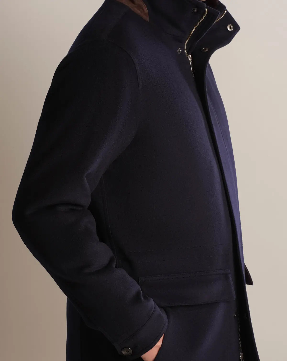 A side view of a person wearing a Cavour Navy Winter Car Coat with Removable Cashmere Collar. The wool-blend design features a high collar with a brown inner lining, a silver zipper, a button-snap closure at the neck, and large flap pockets at the hip. , available at Richard Gelding Mayfair