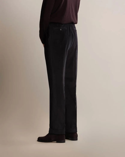 A side view of a person wearing navy Cavour Navy Wide Leg Pleated Corduroy Trousers with a dark maroon long-sleeved shirt and dark brown loafers against a plain, light-toned studio background. , available at Richard Gelding Mayfair