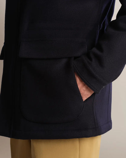 A close-up of a navy wool-blend Cavour Navy Winter Car Coat with Removable Cashmere Collar, highlighting the felted texture and a large, flap-covered rectangular patch pocket with a hand tucked inside resting against tan trousers. , available at Richard Gelding Mayfair