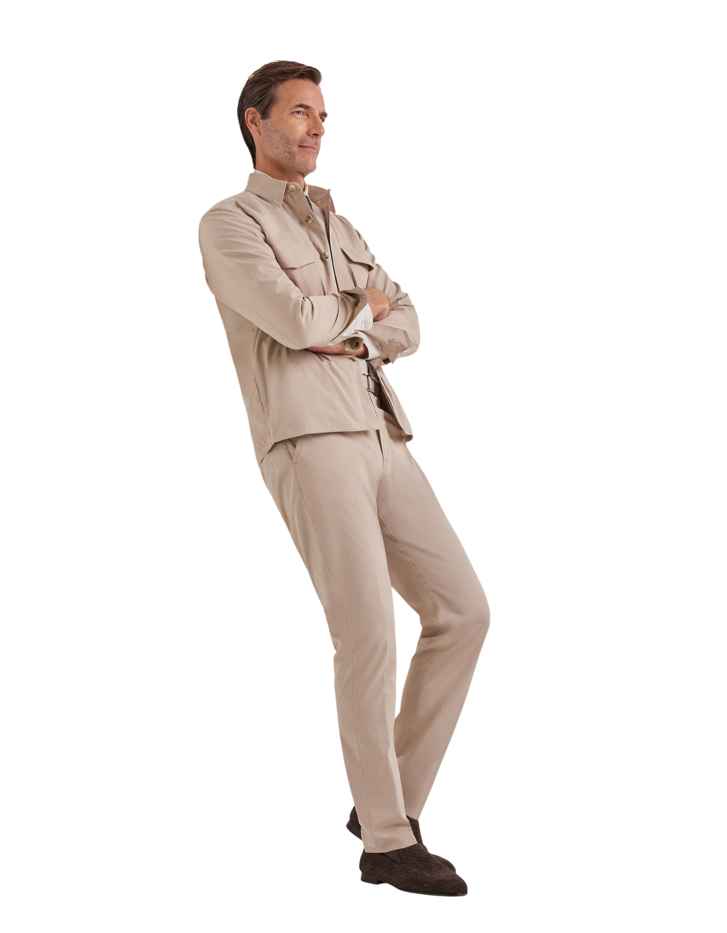 A man stands with arms crossed, smiling slightly and facing left, wearing Canali Beige Cotton Poplin Self-Belt Trouser and a matching beige jacket, paired with dark brown shoes, set against a plain white background. , available at Richard Gelding Mayfair