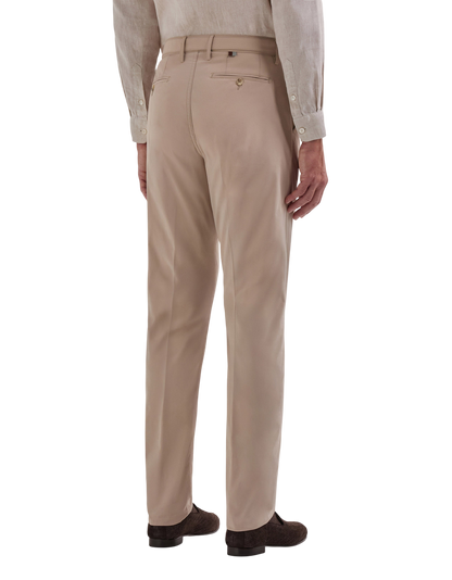 A person stands facing away, wearing Canali Beige Cotton Poplin Self-Belt Trousers with two back pockets—one buttoned, one with a black tag—teamed with a light button-up shirt and dark suede shoes. , available at Richard Gelding Mayfair