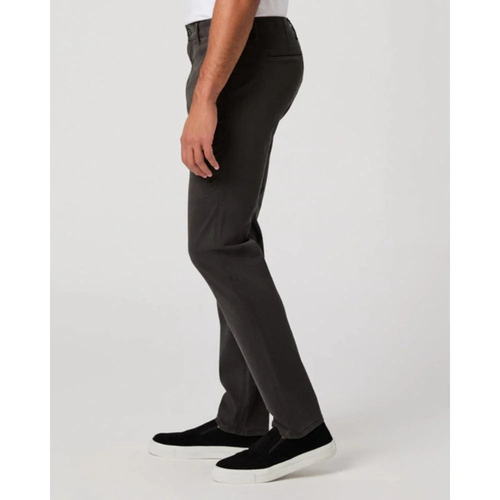 A person stands in profile wearing Paige's Dark Iron Grey Danford Cotton Chino pants. The focus is on the lower body from waist to feet, against a plain light gray background. , available at Richard Gelding Mayfair