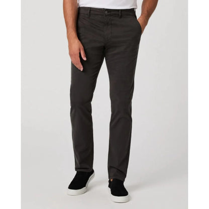 Wearing Paige’s Dark Iron Grey Danford Cotton Chino, a person stands against a plain light background. The straight-fit pants are paired with a tucked white shirt and black slip-on shoes; only the lower torso and legs are shown. , available at Richard Gelding Mayfair