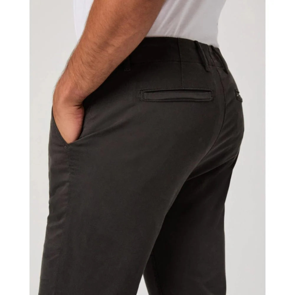 A person wearing Paige Dark Iron Grey Danford Cotton Chino pants and a white shirt is shown from the waist down, side and back view. One hand is in a front pocket, rear welt pockets visible. The background is plain and light-colored. , available at Richard Gelding Mayfair