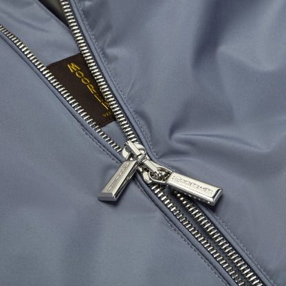 Close-up of the Navy Blueberry Nylon Alcide Blouson by Moorer—a lightweight, navy jacket with shiny fabric, featuring a partially unzipped silver zipper and a glimpse of the brown inner label with yellow text in classic retro blouson style. , available at Richard Gelding Mayfair