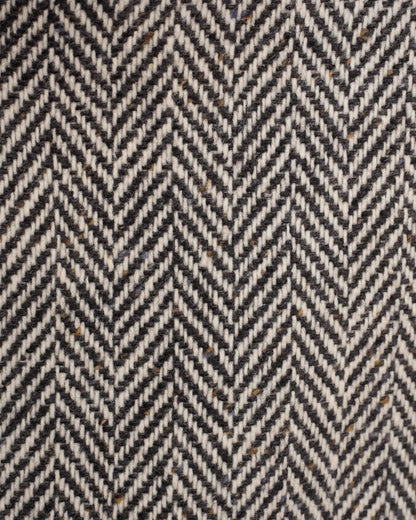 A close-up of the Black Raglan Tweed Coat in heavy wool with a black and white herringbone pattern, featuring subtle flecks of brown and blue woven throughout the textured fabric. , available at Richard Gelding Mayfair